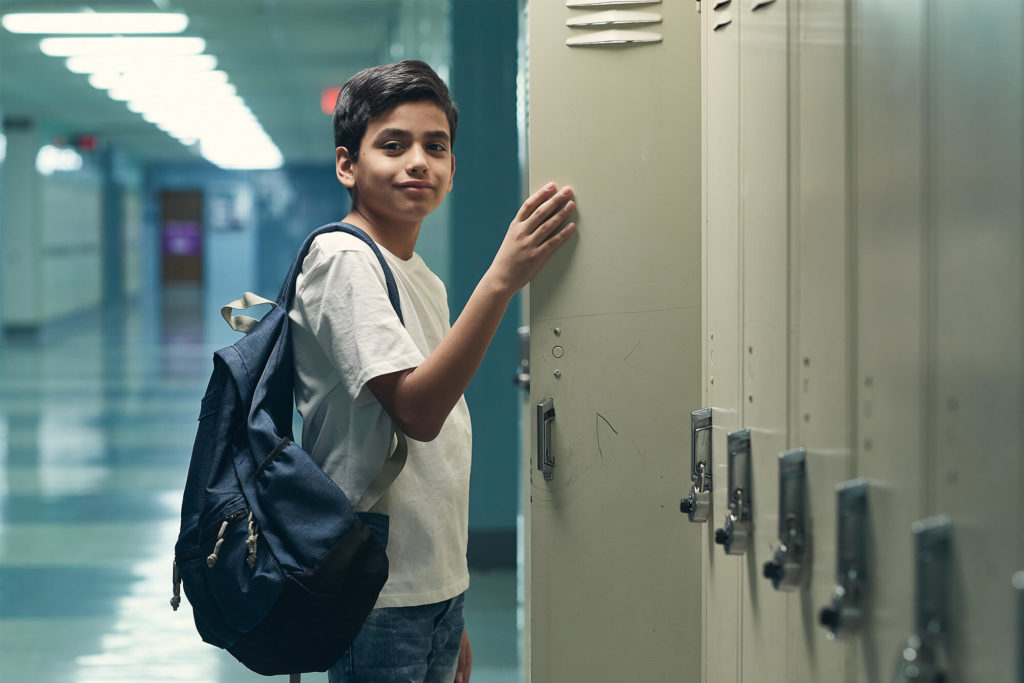 Teen boy standing at an open locker in a school hallway